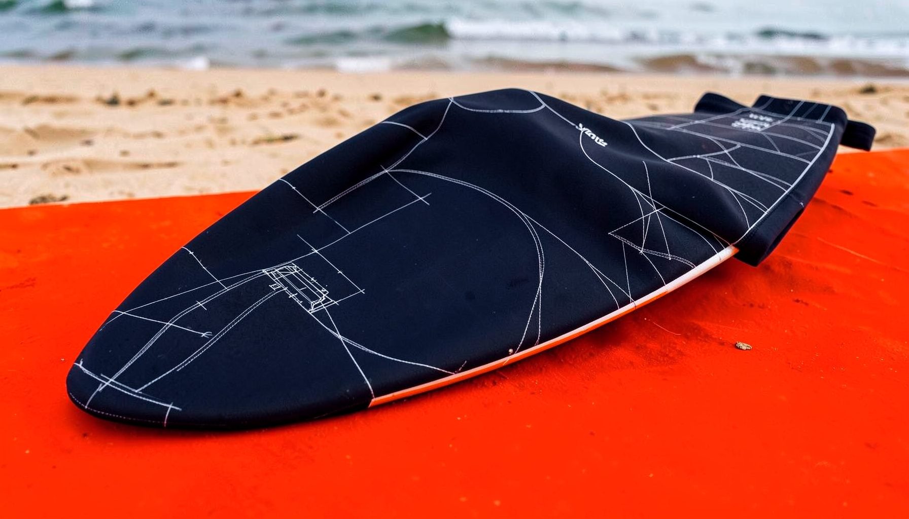 A neoprene wetsuit draped over a surfboard against a sandy beach backdrop, deep navy and charcoal tones